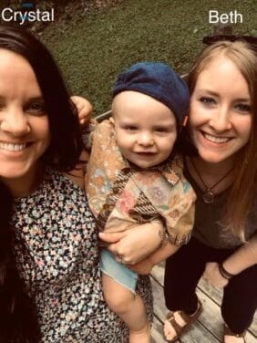 Two women, Crystal and Beth, smile at the camera while one holds a baby outdoors.